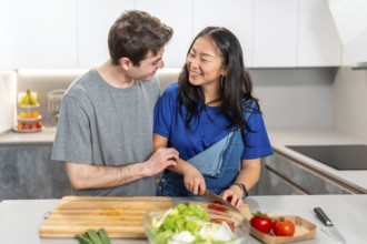 Multiethnic couple sharing a joyful moment while preparing a meal in a sleek, modern kitchen. Fresh