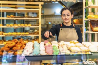 Latin young woman wearing apron selling artisan pastries in a bakery