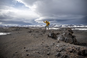 Hiker jumps into the air, snow-covered volcanic landscape with volcanic sand and petrified lava,