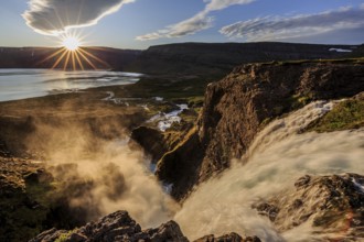 Waterfall backlit by midnight sun in front of mountains and coast, summer, Dynjandi, Westfjords,
