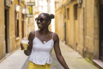 Happy african young woman drinking a iced milkshake while walking along a street