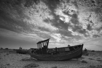Broken discarded fishing boats on a shingle beach against a dramatic cloudy backdrop, boat