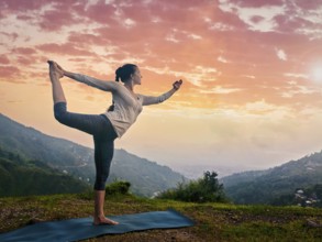 Woman doing yoga asana Natarajasana, Lord of the dance pose outdoors at waterfall in Himalayas