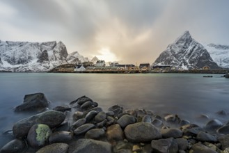 Traditional yellow rorbuer cabins on Sakrisøy Island, snow-capped rocky mountains in the back,