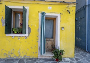 Yellow house facade with entrance door with green and white curtain and windows, colourful houses