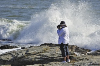 Tourist taking pictures of waves crashing on the rocks at the Pointe Saint-Gildas, Saint Gildas