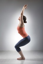 Sporty fit woman doing Surya Namaskar ashtanga vinyasa yoga asana Utkatasana, chair pose