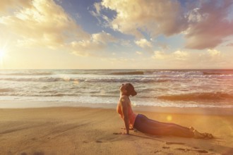 Yoga outdoors on beach, woman practices Ashtanga Vinyasa yoga Surya Namaskar Sun Salutation asana