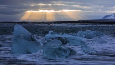 Waves breaking on icebergs on the black beach of Breidamerkursandur, sunset, near Jökullsarlon,
