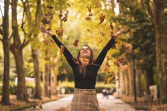 Portrait of a woman in autumn in a forest with brown leaves at sunset in a city park, throwing