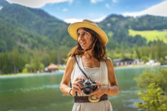 Woman wearing straw hat holding vintage camera enjoying breathtaking view of lake dobbiaco and
