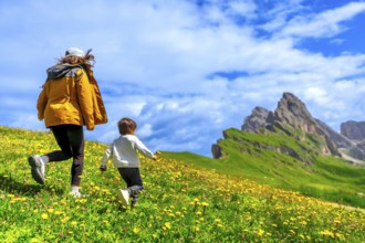 Tourists running on a flowery meadow with the odle and seceda mountains in the background,