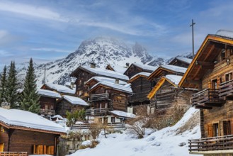Old snow-covered wooden houses in the historic village centre, with the snow-covered summit of the