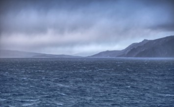 View of Cape Horn in the haze under a dramatic sky with distant coastlines, Chile, South America