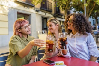 Women toasting and celebrating together sitting on an outdoor bar during sunset in the city
