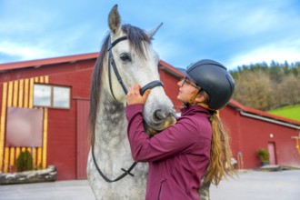 Female young jockey with helmet caressing a horse head on a equestrian center