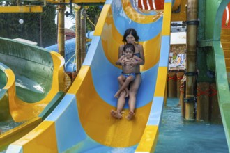 A woman and a child are sliding down a water slide. The slide is yellow and blue