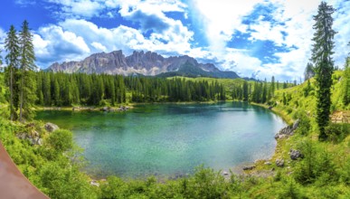 Emerald green water of lake carezza reflecting latemar mountain range in italian dolomites,