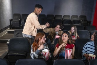 Young people enjoying a movie night out at the cinema, greeting each other and eating popcorn