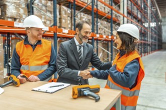 Manager shaking hands with a smiling female worker in a logistics warehouse, a male worker is