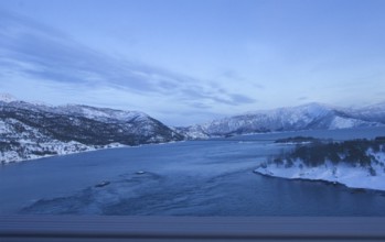 View of a river surrounded by snowy mountains under a clear blue sky, Norway, Europe