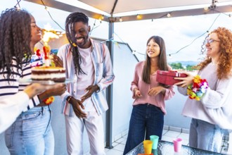 African happy woman receiving a gift and birthday cake celebrating with multi-ethnic friends in a
