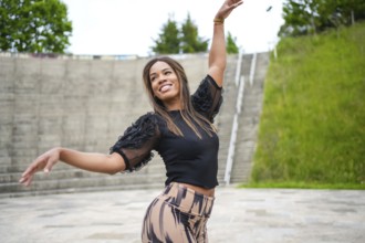 Latin smiling young woman enjoying dancing salsa alone in a park