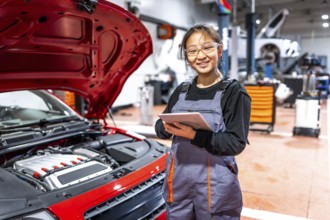 Confident female mechanic using a digital tablet, inspecting a car engine in a professional auto