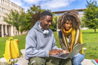 Two multi-ethnic students using laptop sitting outside the campus