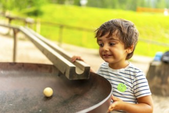 Curious child having fun with a wooden ball rolling down a track in a playground, learning about