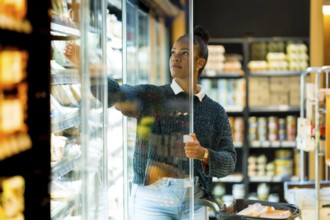 Customer selecting groceries from refrigerated section in a supermarket, holding shopping cart