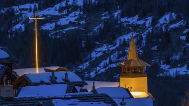 Illuminated Saint Theodule church and illuminated cross in wintery Grimentz, Val d'Anniviers,