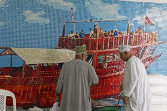 Omani men in dishdashas in front of the wall mosaic of a ship in Muttrah Fish Market, Muscat, Oman,