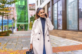 African businesswoman walking while talking to the mobile phone along a city street with fallen