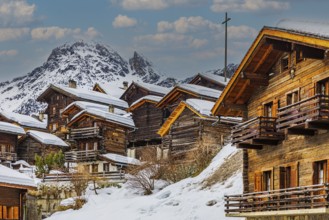 Old snow-covered wooden houses in the historic village centre, with the snow-covered summit of the