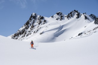 Ski tourer on the descent, minimalist winter landscape, white snow and dark mountains on the