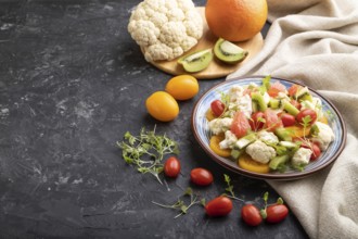 Vegetarian salad of cauliflower cabbage, kiwi, tomatoes, microgreen sprouts on black concrete