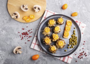 Stuffed fried champignons with cheese, kumquats and green peas on a gray concrete background.