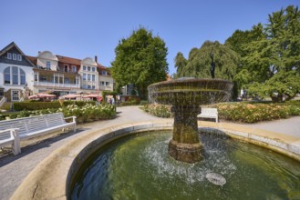 Fountain with benches, trees and houses under a cloudless blue sky in Bad Salzuflen, Lippe