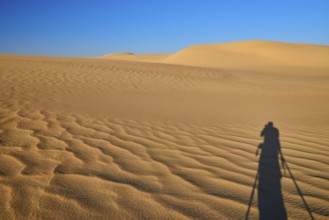 Shadow of a photographer in a vast desert landscape with sand dunes and blue sky, Matruh, Great