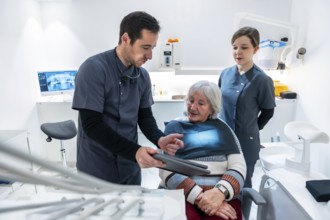 Dentist and nurse explaining radiography to a senior patient sitting in a dental chair, during a