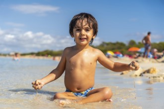 Happy child playing with sand sitting on the shore of a paradisiacal beach with crystalline waters