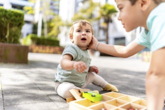 Close-up of a bother caressing a baby boy playing with toys in a park