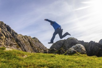 Male hiker jumping on a green meadow in front of the rocky peaks of aiako harria or penas de aia