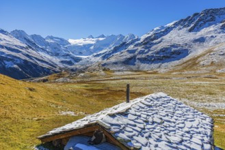 Alpine hut with snow-covered roof, slightly snow-covered alpine meadow, behind the Moiry glacier,