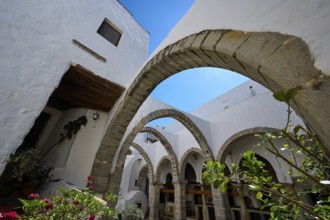 Inner courtyard with stone arches, plants and white walls under a blue sky in a Mediterranean