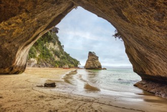 Looking out of a cave onto a rock formation and a quiet beach, Cathedral Grove, Coromandel, New