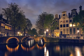 Night view of Amterdam cityscape with canal, bridge and medieval houses in the evening twilight