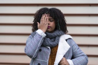 Black ethnic woman making a stop racism gesture on a gray wall, covering her eyes