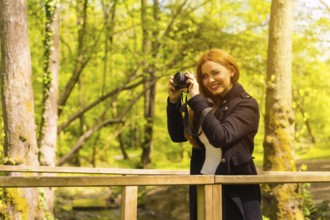 Woman photographer with a black jacket enjoying in an autumn park, taking pictures at sunset on a